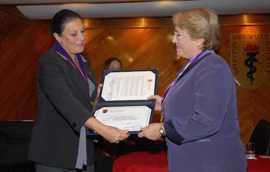 Figura 6: León-Velarde presentando a la Directora Ejecutiva de la ONU, Michelle Bachelet con un doctorado honorario de la Universidad Peruana Cayetano Heredia en el año 2012.